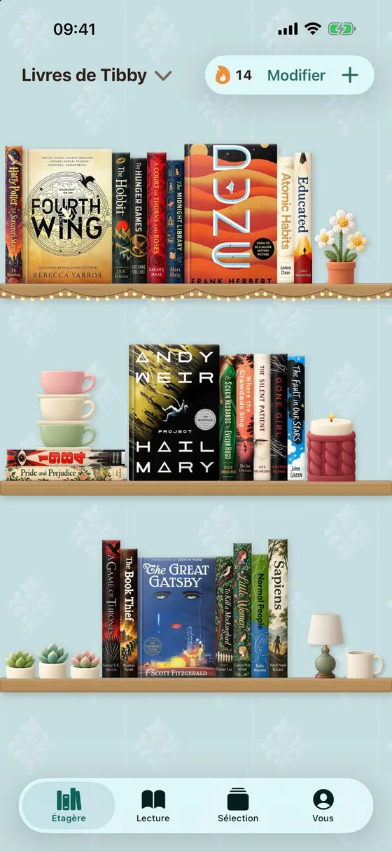 Une étagère décorée dans Tibby, sur un mur bleu canard à motifs : Fourth Wing, Dune et Project Hail Mary, avec des tasses, une bougie tricotée et des plantes.